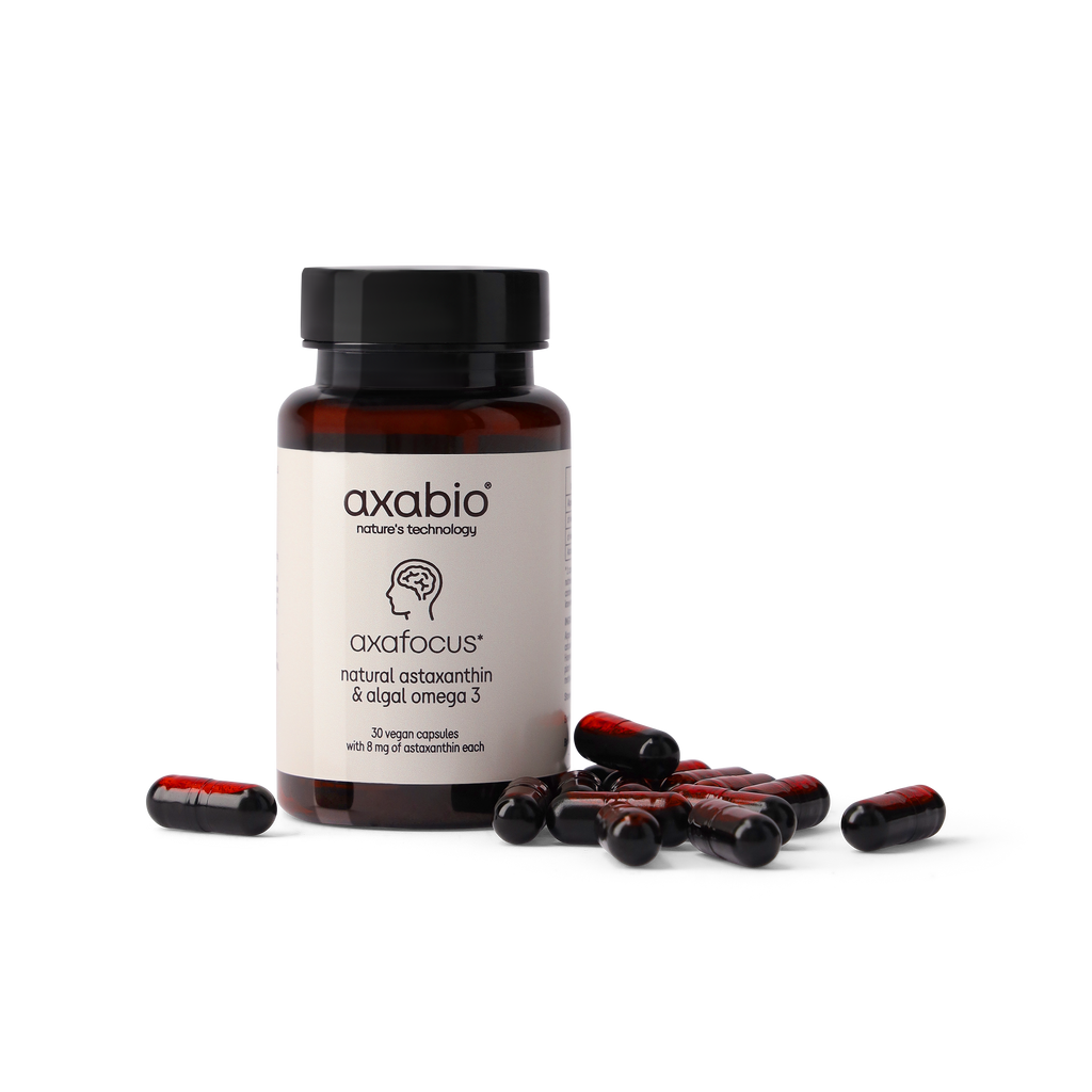 A bottle of axabio Axafocus dietary supplement capsules with several red and black capsules scattered in front, set against a solid white background.