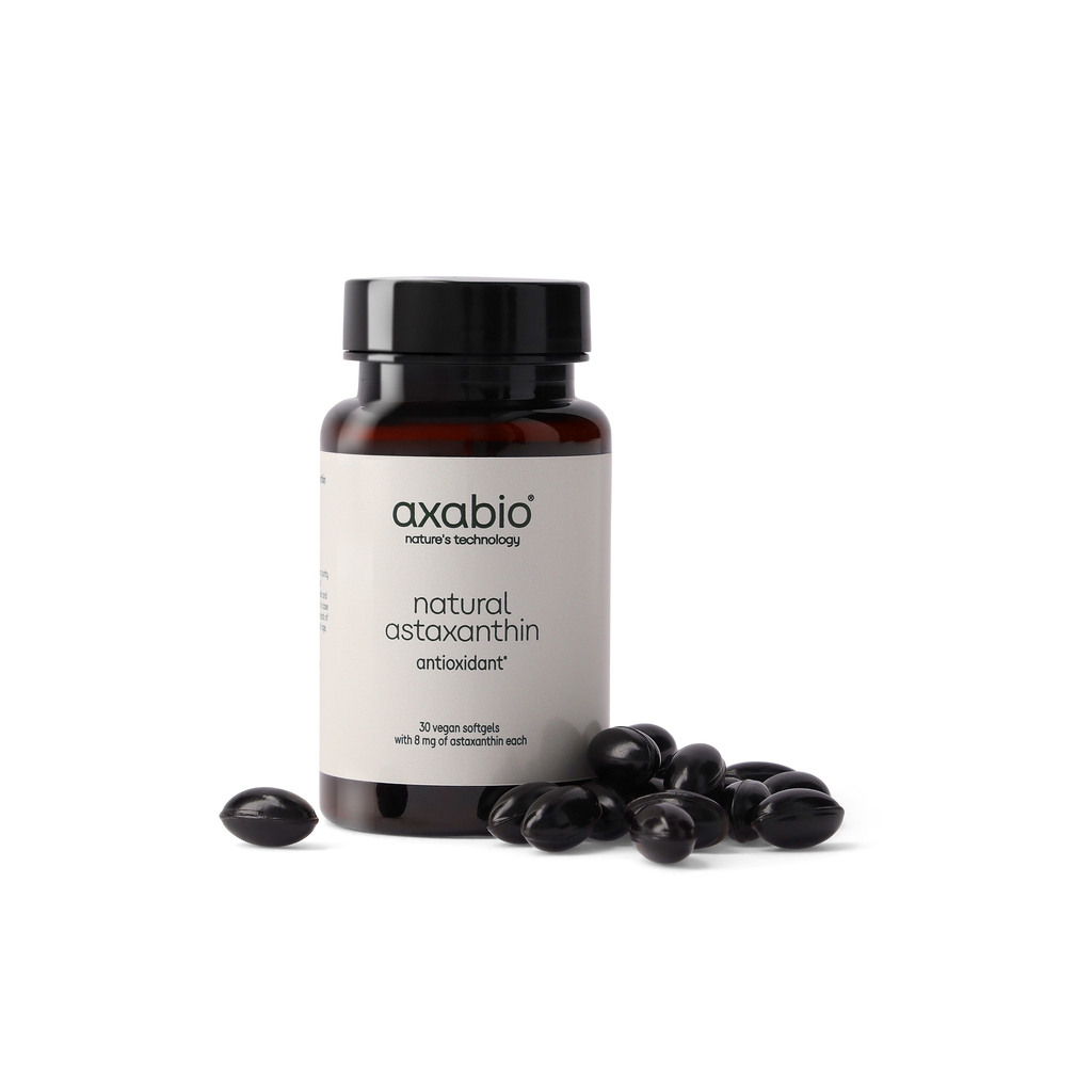 A bottle of axabio natural astaxanthin dietary supplement with a black cap and white label, shown on a white background with several dark astaxanthin crystals in front of the bottle.