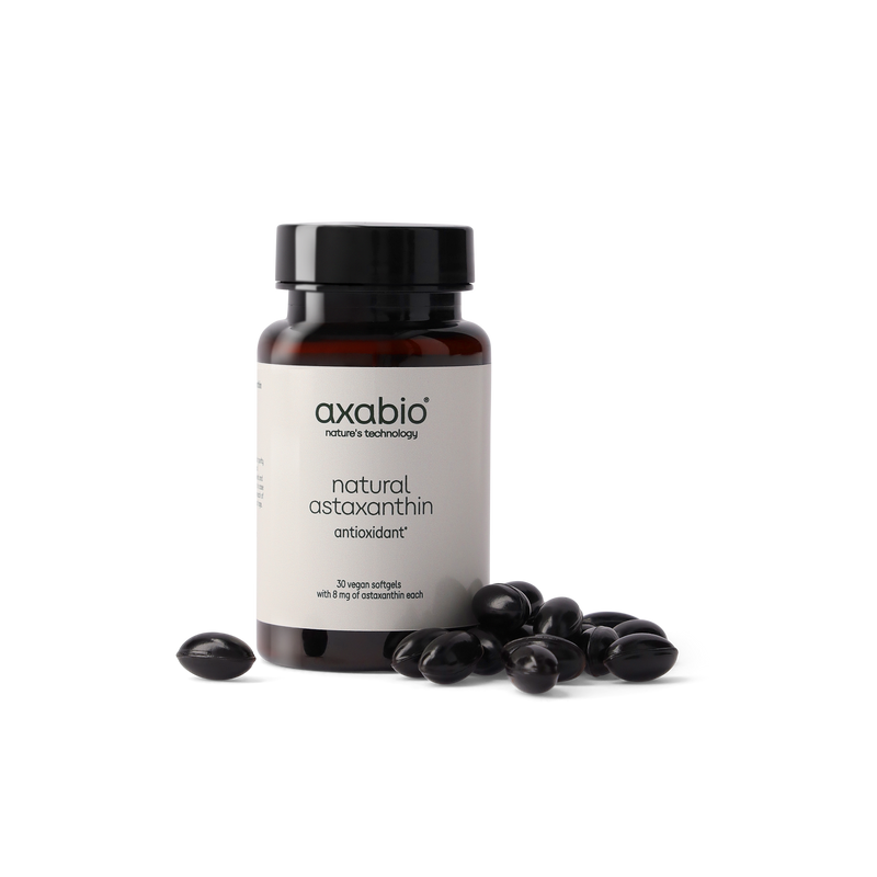 A bottle of axabio natural astaxanthin dietary supplement with a black cap and white label, shown on a white background with several dark astaxanthin crystals in front of the bottle.