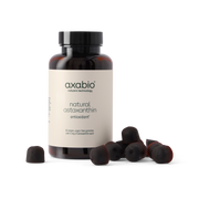 A bottle of axabio natural astaxanthin antioxidant supplement with several dark red astaxanthin capsules scattered in front, set against a solid white background.