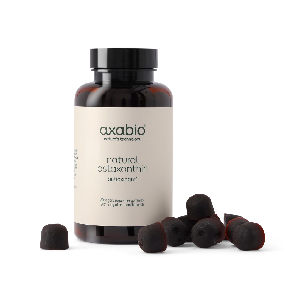 A bottle of axabio natural astaxanthin antioxidant supplement with several dark red astaxanthin capsules scattered in front, set against a solid white background.